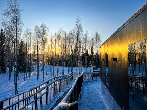 a building in the snow with the sun in the background at Silver Birch Resort Lapland in Rovaniemi