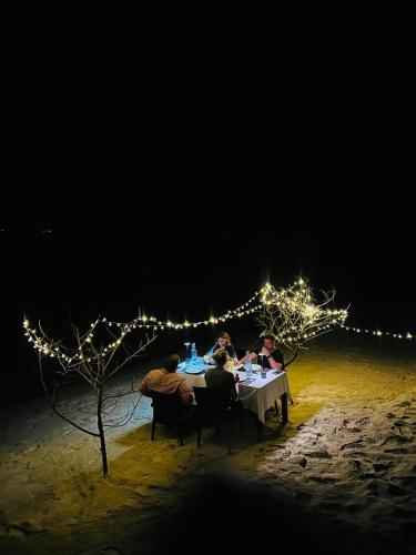 a group of people sitting at a table on the beach at night at Nika Inn Himandhoo in Himandhoo 