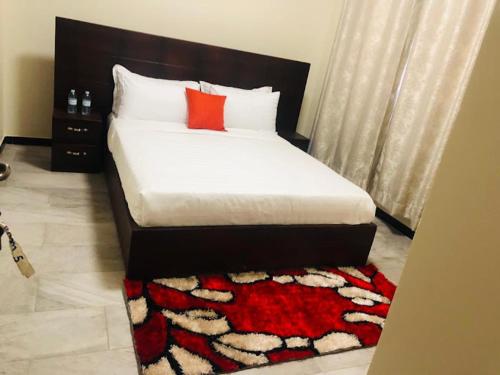 a bedroom with a bed with a red pillow and a rug at SONKOYAZ BED AND BREAKFAST Near UN BASE in Entebbe