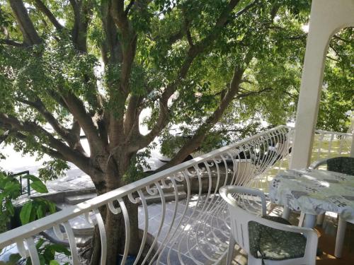 a porch with white tables and chairs and a tree at Apartmani Kristina in Drvenik