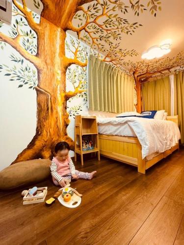 a baby sitting on the floor in a bedroom with a tree mural at 8Home Kids House in Osaka