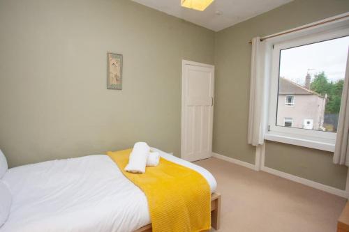 a bedroom with a bed with a yellow blanket and a window at 3 Bed Cottage Flat with Parking in Glasgow