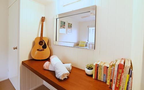 a shelf with books and a guitar and a mirror at Little Gem in Peregian Beach - walking distance to beach with pool in Peregian Beach