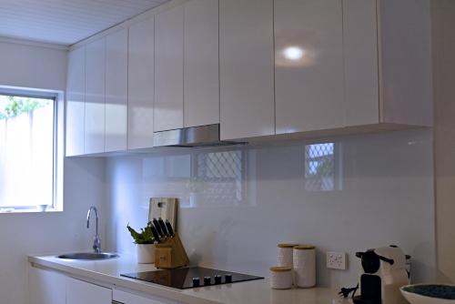a white kitchen with white cabinets and a sink at Little Gem in Peregian Beach - walking distance to beach with pool in Peregian Beach