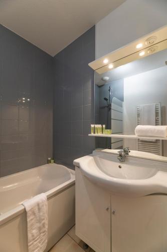 une salle de bain avec un lavabo, une baignoire et un miroir dans l'établissement Lagrange Vacances L'Estuaire, au Le Verdon-sur-Mer