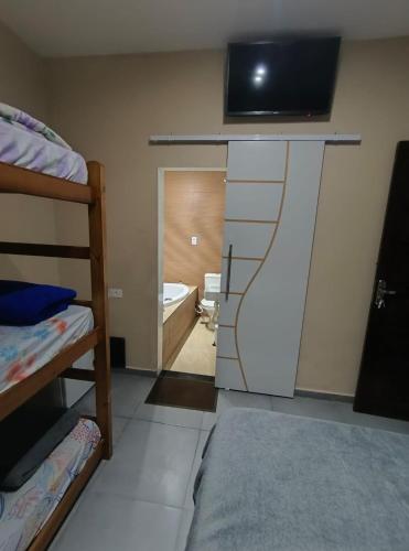 a room with a tv on the wall and a bedroom at Pousada chc in Praia Grande