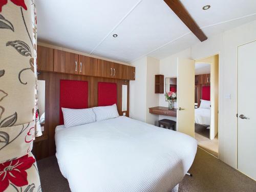 a bedroom with a white bed with a red headboard at TOM TODDY - Enchanting Golden Sands Caravan at Dawlish Warren in Dawlish Warren