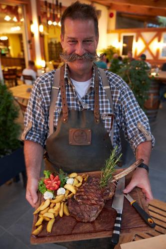 a man with a beard holding a plate of food at Flair Hotel Landgasthof Roger in Löwenstein