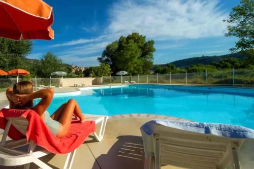 une femme assise sur une chaise à côté d'une piscine dans l'établissement Camping Bel Air Village Les Prés du Verdon, à Quinson