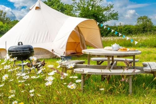 a tent and a picnic table in front of a field of flowers at Red Clover at Blancas Bell Tents in Ringstead