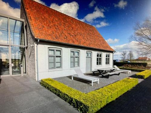 a white building with an orange roof and two benches at SCHRAVENHOEk met indoorzwembad en sauna in Veurne