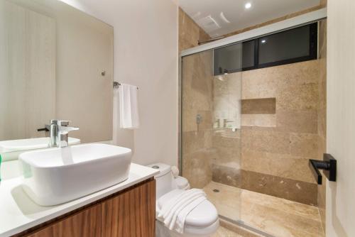 a bathroom with a toilet and a sink and a shower at Aldea Zama 2-BR Lux Building Amenities in Tulum