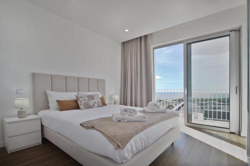 a white bedroom with a large bed and a large window at Like Home I - vista mar e ambiente relaxante in Funchal