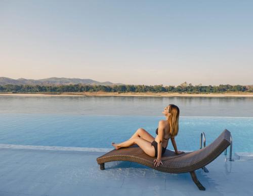 a woman sitting on a bench next to the water at Chiangkhan River Mountain Resort in Chiang Khan