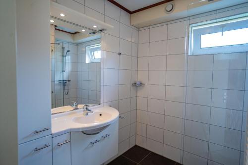 a white bathroom with a sink and a mirror at Vakantiehuis Hoogelandt 134 en 134a in De Koog