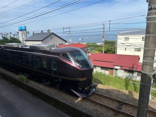 a black train traveling down the tracks near buildings at 窓際から海と鉄道が見える宿 サウナ プロジェクター カラオケ完備 トリックマーメイド in Ito