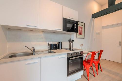- une cuisine avec des placards blancs, un évier et des chaises rouges dans l'établissement Studio sous les combles côté cour, parking gratuit, à Villeneuve d'Ascq