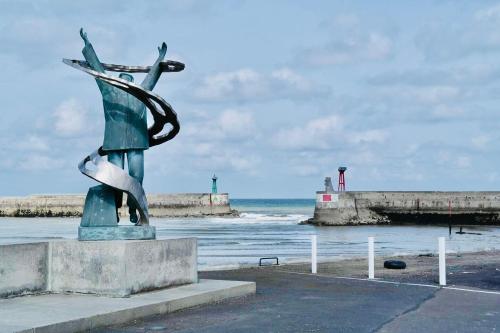 a statue in front of the ocean with a pier at Vue Sur Mer in Port-en-Bessin-Huppain