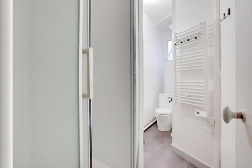 La salle de bains blanche est pourvue de toilettes et d'une porte en verre. dans l'établissement Studio Lumineux au pied du RER A - Avec ascenseur, à Vincennes