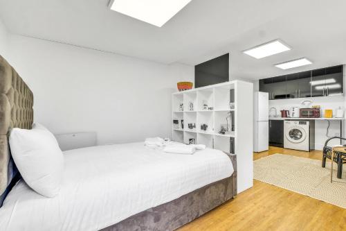 a bedroom with a large white bed and a kitchen at Detached & Secluded Bungalow, Northern Line 20m to Central London, Marathon and Events ready in Colindale