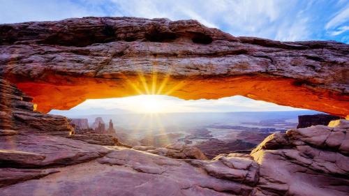an arch in the desert with the sun shining through it at Downtown Hideaway in the Heart of Moab in Moab