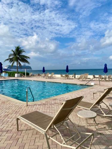a swimming pool with chairs and the ocean in the background at Oceanfront Condo on Seven Mile Beach in Dog City