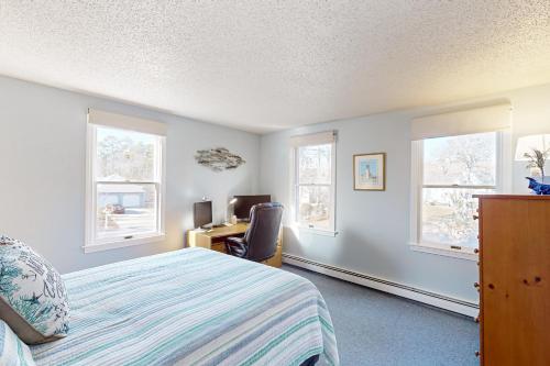 a bedroom with a bed and a desk and windows at National Seashore Retreat in Eastham