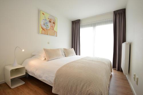 a bedroom with a white bed and a window at Residentie Rivella in Koksijde