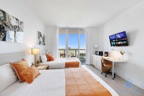 a hotel room with two beds and a desk and a window at Amazing Balcony Near Beach in Hallandale Beach
