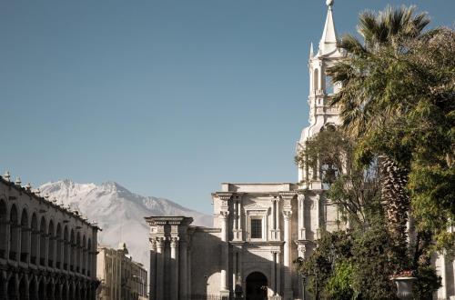 a building with a clock tower with a mountain in the background at CIRQA - Relais & Châteaux in Arequipa