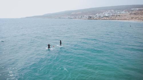 two people are riding on surfboards in the ocean at Appartement Taghazout in Taghazout