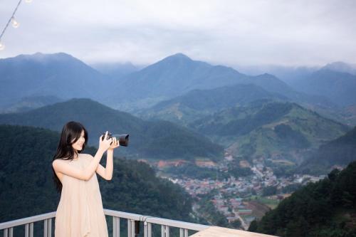 a woman taking a picture of the mountains with a camera at Mây home Trạm Tấu lều khách sạn in Ya Ló