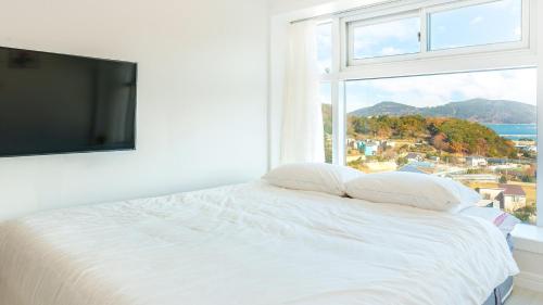 a bedroom with a white bed with a large window at Geoje Forest-Morning Spa Pension in Geoje 