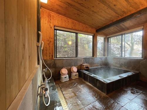 a large bath tub in a room with windows at Kurasako Onsen Sakura in Minamioguni