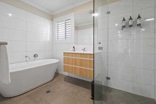 a white bathroom with a tub and a shower at Thane Retreat - Cosy Ambience, Modern Entertaining in Wagga Wagga