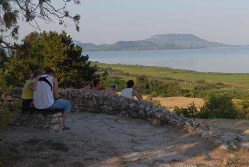 people sitting on a stone wall looking at the water at Hotel Panoráma in Balatongyörök
