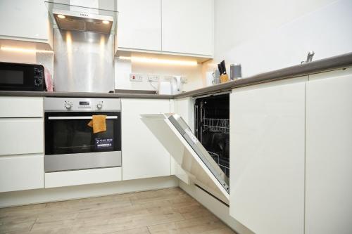 a kitchen with white cabinets and an open dishwasher at Luxury Ensuite Apartment with shared living room and kitchen in Manchester