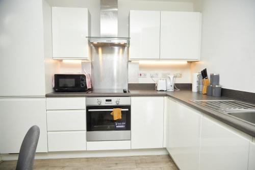 a kitchen with white cabinets and a stove top oven at Luxury Ensuite Apartment with shared living room and kitchen in Manchester