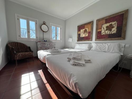 a white bedroom with two beds and a chair at Una casita en el campo dentro de la ciudad in Avila