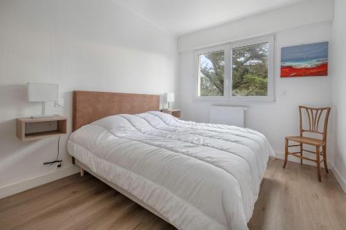 a white bedroom with a large bed and a chair at Vue mer - appartement pour 2 au Croisic in Le Croisic