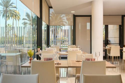 Un restaurante con sillas y mesas blancas y ventanas. en Catalonia Barcelona Beach, en Barcelona