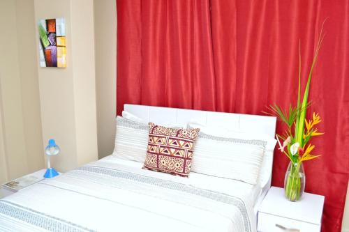 a bedroom with a white bed with a red curtain at Acquah Place Residences in Accra