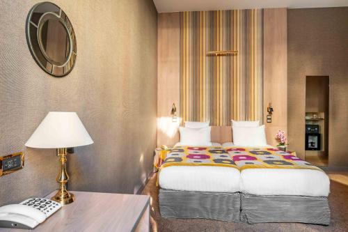 a bedroom with a bed and a table with a lamp at Hôtel Regent's Garden - Astotel in Paris