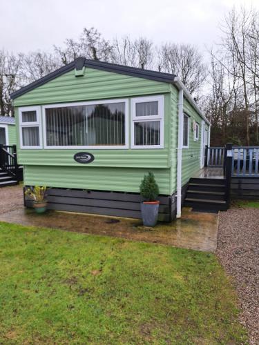 a green tiny house sitting on a wooden deck at 11 Borwick Lakes in Carnforth