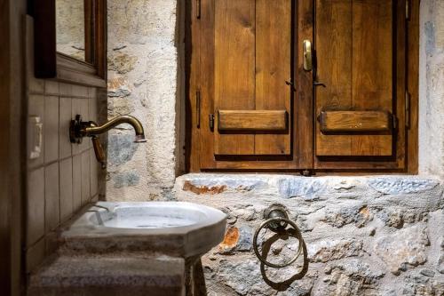 a stone bathroom with a sink and a wooden door at Tzokeika Traditional Settlement in Riglia