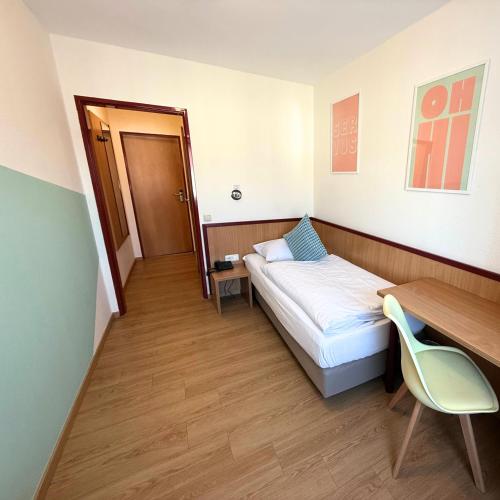 a small room with a bed and a desk and a chair at Colourful Hotel in Bielefeld