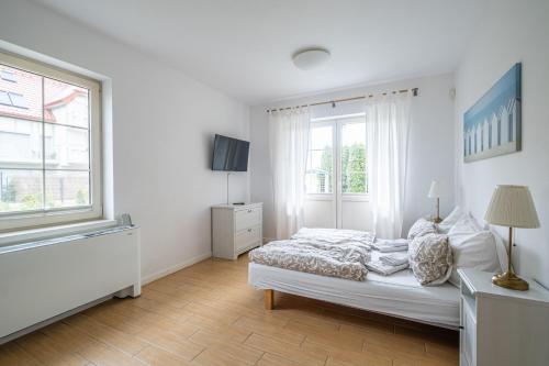 a white bedroom with a bed and a window at Dębki Playa Apartments in Dębki