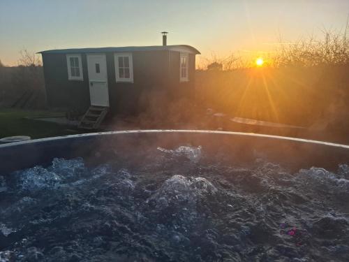 a hot tub in front of a house with the sunset at Hill Top Hideaway Shepherds Hut with Hot Tub in Woodham Mortimer