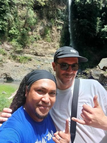 two men standing next to each other in front of a waterfall at Kristian Homestay in Bajawa