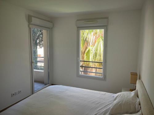 une chambre blanche avec un lit et deux fenêtres dans l'établissement 2 Bedroom Apartment Near Beach, à Mandelieu-la-Napoule